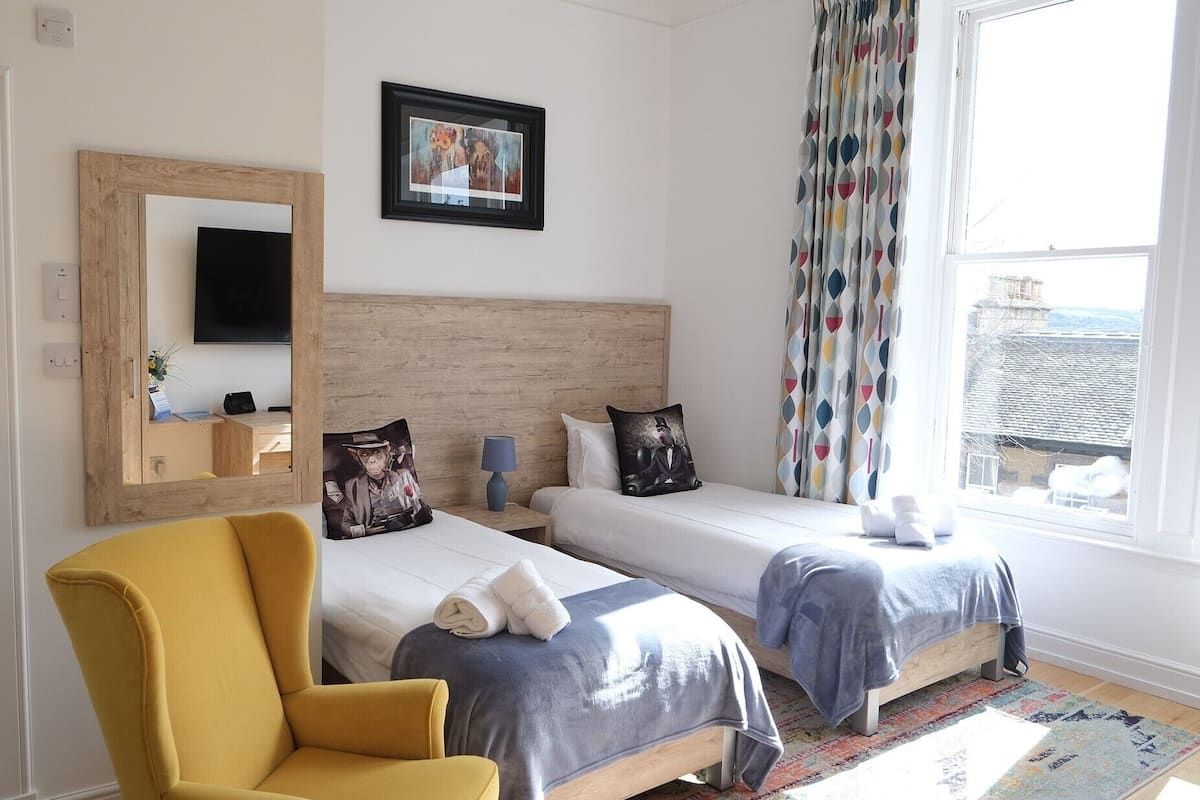 A bedroom with two beds, a mirror, a chair, and a window with curtains.