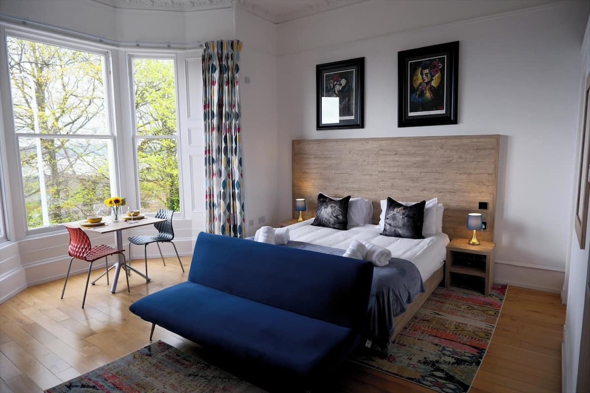 A bedroom with a bed, a blue sofa, a desk with a chair, and two bedside tables with lamps.