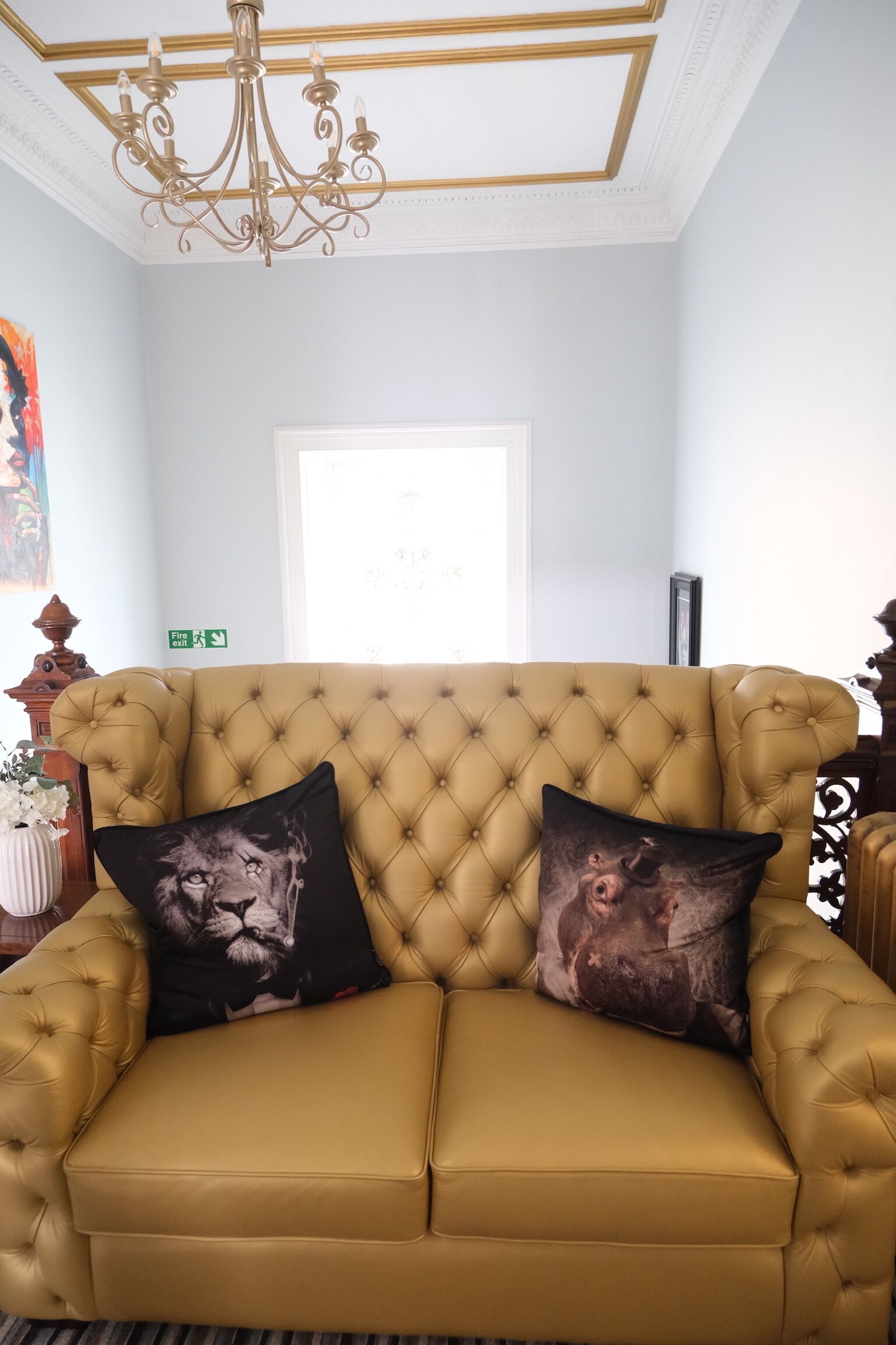 A tufted sofa with two decorative pillows, a chandelier, and a framed artwork on the wall.