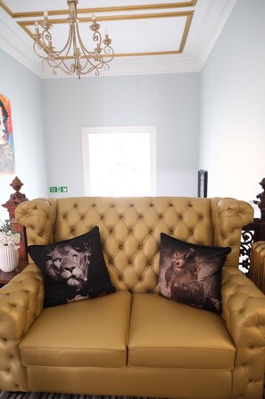 A tufted sofa with two decorative pillows, a chandelier, and a framed artwork on the wall. - The Clarendon (Dundee)