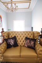 Un sofá capitonado con dos almohadones decorativos, una araña y una obra de arte enmarcada en la pared.