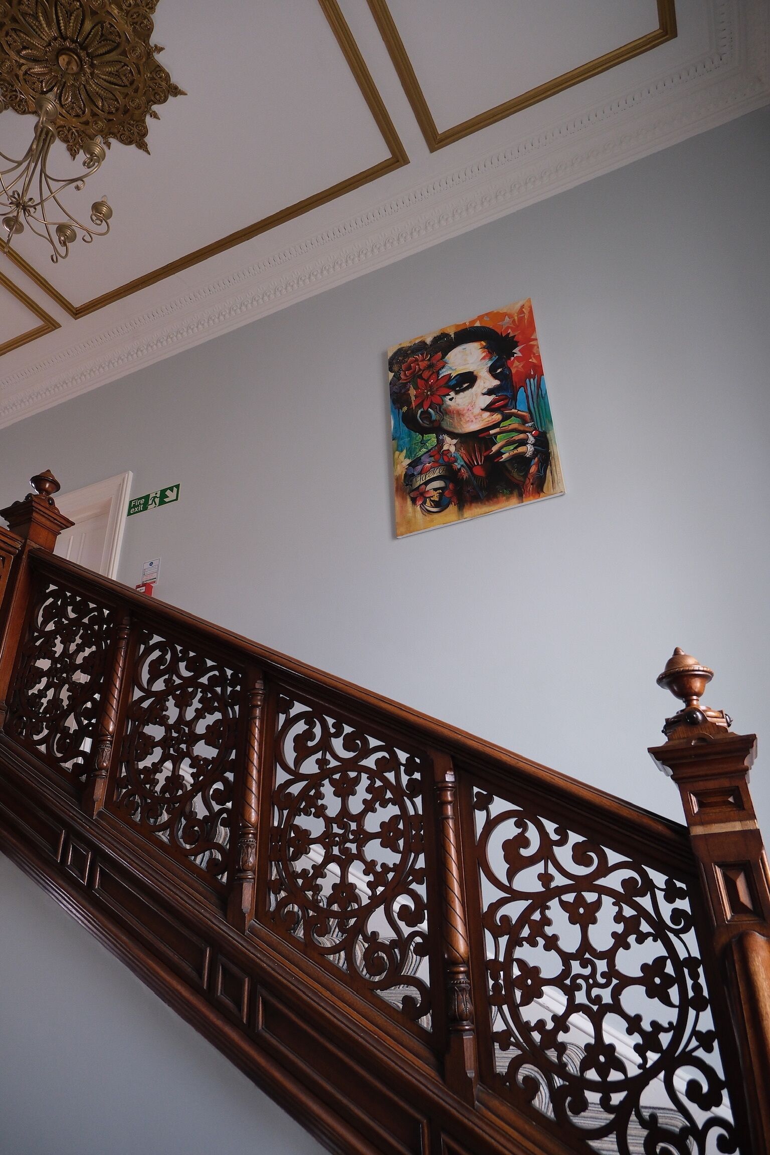 Una escalera con barandillas de madera decoradas y un techo con molduras ornamentales.