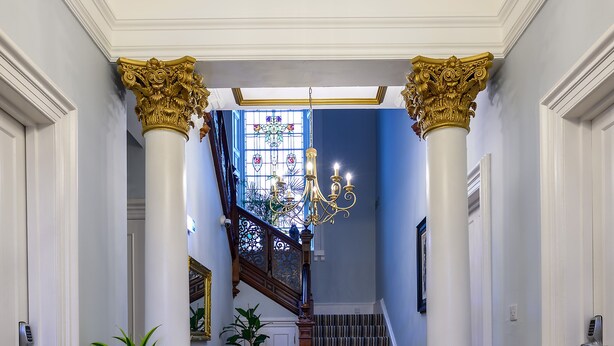 A grand hallway with a yellow armchair, a striped rug, and a staircase leading to a balcony. - The Clarendon (Dundee)