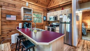 A wooden cabin interior with a kitchen featuring a central island, bar stools, a refrigerator, and a microwave. - Book for fall now! Enjoy our hot tub and deck! (Gatlinburg)
