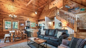 A cabin interior with a wooden ceiling, a dining area with rustic furniture, a living room with a sofa and a coffee table, and a kitchen with modern appliances. - Book for fall now! Enjoy our hot tub and deck! (Gatlinburg)
