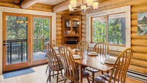 A wooden cabin interior with a dining area, bookshelves, and large windows. - Custom Log Cabin with Great Amenities! (Leavenworth)