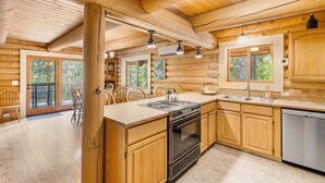 A wooden cabin interior with a kitchen, dining area, and large windows. - Custom Log Cabin with Great Amenities! (Leavenworth)