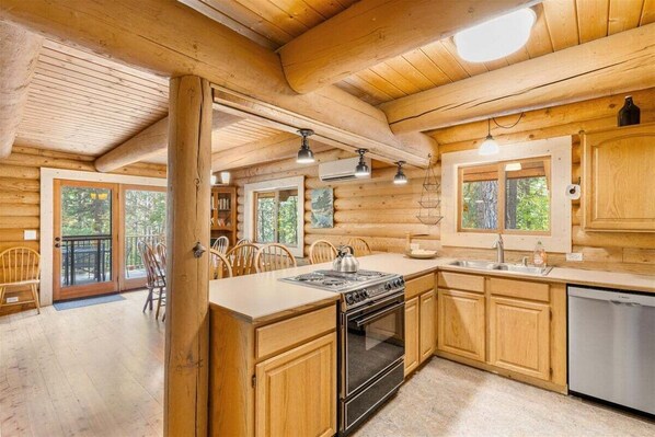 A wooden cabin interior with a kitchen, dining area, and large windows. - Custom Log Cabin with Great Amenities! (Leavenworth)