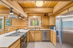 A log cabin kitchen with wooden cabinets, a stainless steel refrigerator, a microwave, a sink, and a stove.
