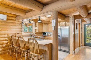 A log cabin interior with a kitchen island, bar stools, a refrigerator, and wooden cabinets.