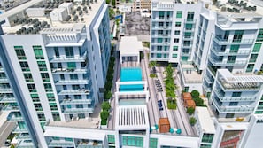 Un moderno edificio de gran altura con varios balcones, una piscina central y una terraza en la azotea con mobiliario exterior.