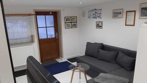 Un salon avec un canapé, une table basse et un téléviseur. Il y a une porte avec une fenêtre, et les murs de la pièce sont blancs et ornés de tableaux encadrés.
