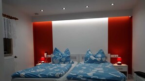 Une chambre avec deux lits, chacun agrémenté de draps bleus et d’oreillers à motifs de cœurs, de têtes de lit blanches et de murs d’accent rouge.
