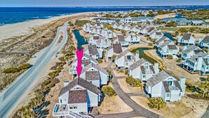 Una zona residencial costera con casas alineadas a lo largo de una calle, una playa y una masa de agua.