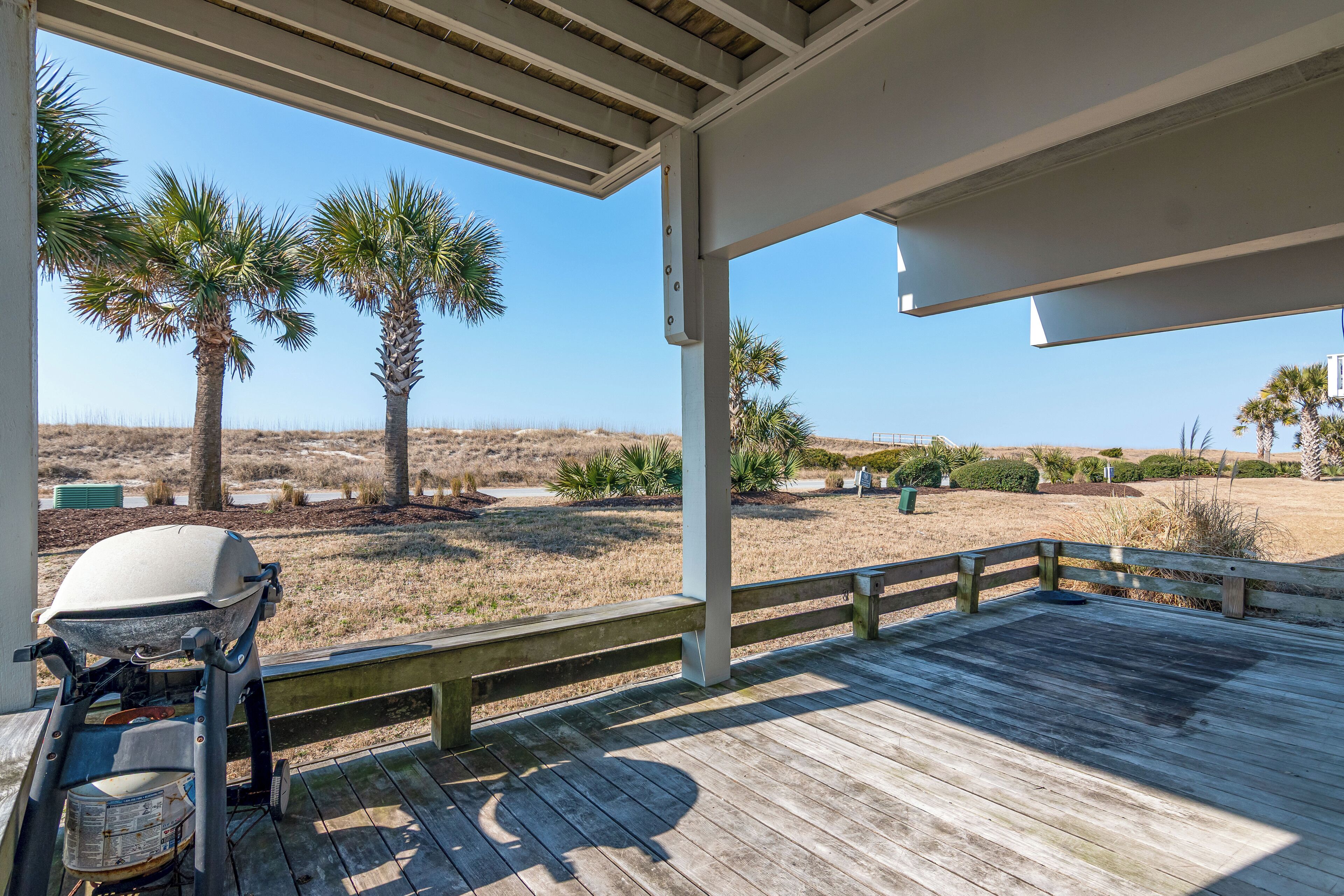 A covered outdoor area with a grill, wooden deck, and palm trees.