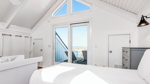 Un dormitorio con una cama grande, un armario, un escritorio y vistas a la playa a través de una puerta corredera.