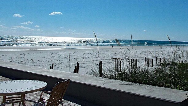 A beach view with a table and chairs, a concrete wall, and a wooden fence. - 202 - Adorable 1 bedroom unit - sleeps 6 (New Smyrna Beach)
