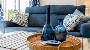 Un salon avec un canapé bleu, des coussins à motifs et deux vases bleus posés sur un plateau en osier.