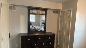 Een slaapkamer met een donkere dressoir, een spiegel, een bed met beddengoed met een patroon, en een witte deur.