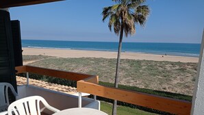 Un balcón con vista a la playa, una palmera, y una mesa y sillas blancas.