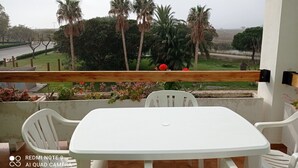 Un balcon avec une table et des chaises blanches, donnant sur un jardin agrémenté de palmiers et de fleurs rouges.