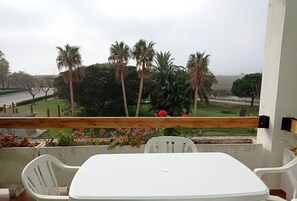 Un balcón con una mesa y sillas blancas, con vistas a un jardín con palmeras y flores rojas.