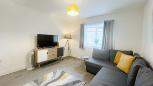 A modern living room with a grey sofa, a flat-screen TV, a lamp, and a floor lamp. - Anstey Heights - Apartment 4 - Hopewell (Easton)