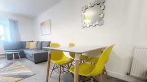 A modern living room with a grey sofa, yellow chairs, a white table, and a decorative mirror on the wall. - Anstey Heights - Apartment 4 - Hopewell (Easton)