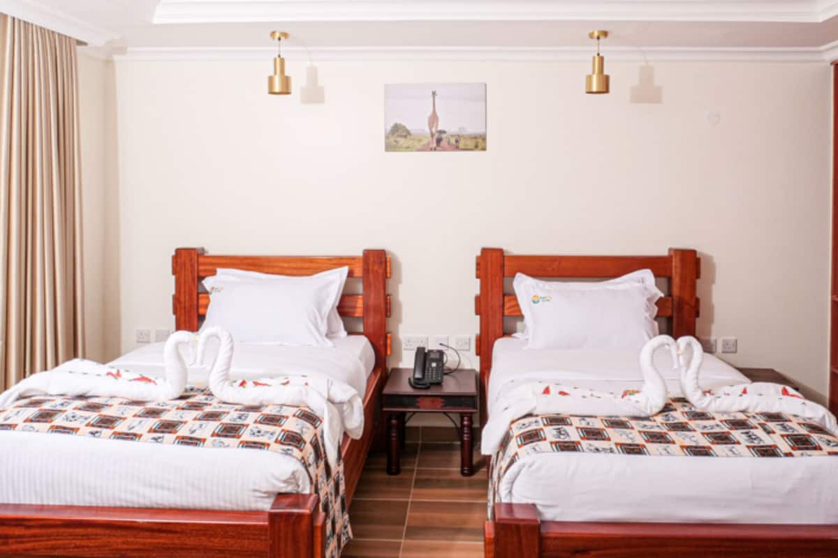 Une chambre d’hôtel avec deux lits en bois, du linge de lit blanc et une petite table de chevet avec un téléphone.