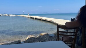 A view from a seaside restaurant with a long pier extending into the water, a person standing at the end, and boats docked nearby. - Villa Alexakis (corfu)