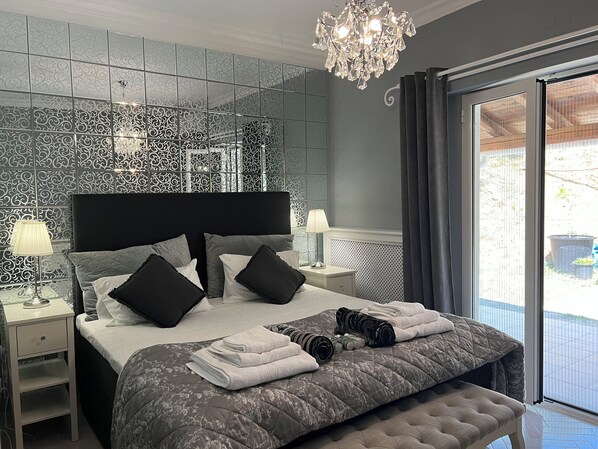 A modern bedroom with a large bed, a chandelier, and a view of the outdoors.