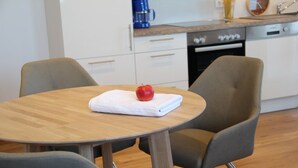 Eine kleine, moderne Küche mit weißen Schränken, einem Holztisch und zwei grauen Stühlen.
