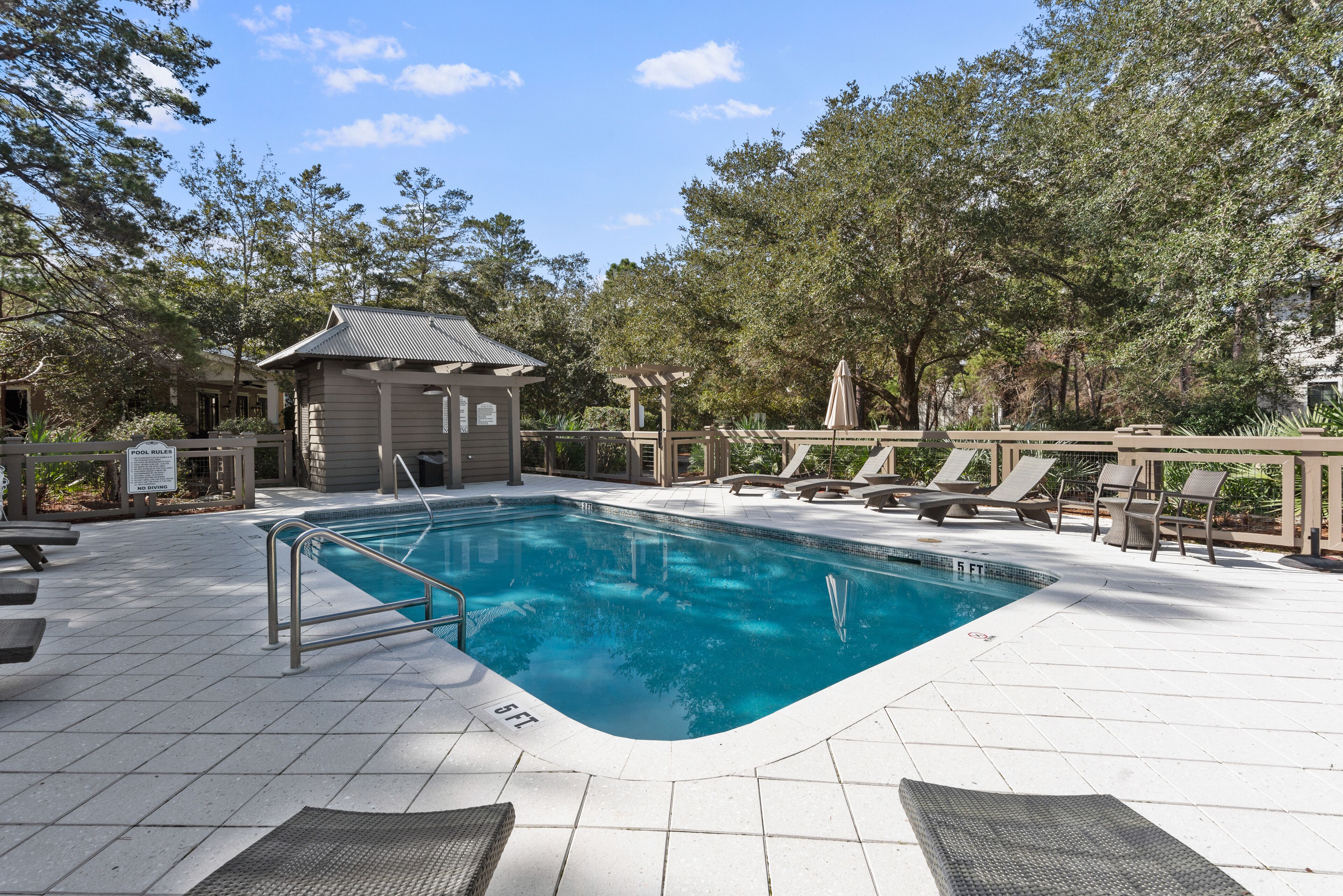 A swimming pool with a 5 ft depth marker, surrounded by lounge chairs and a small pavilion.