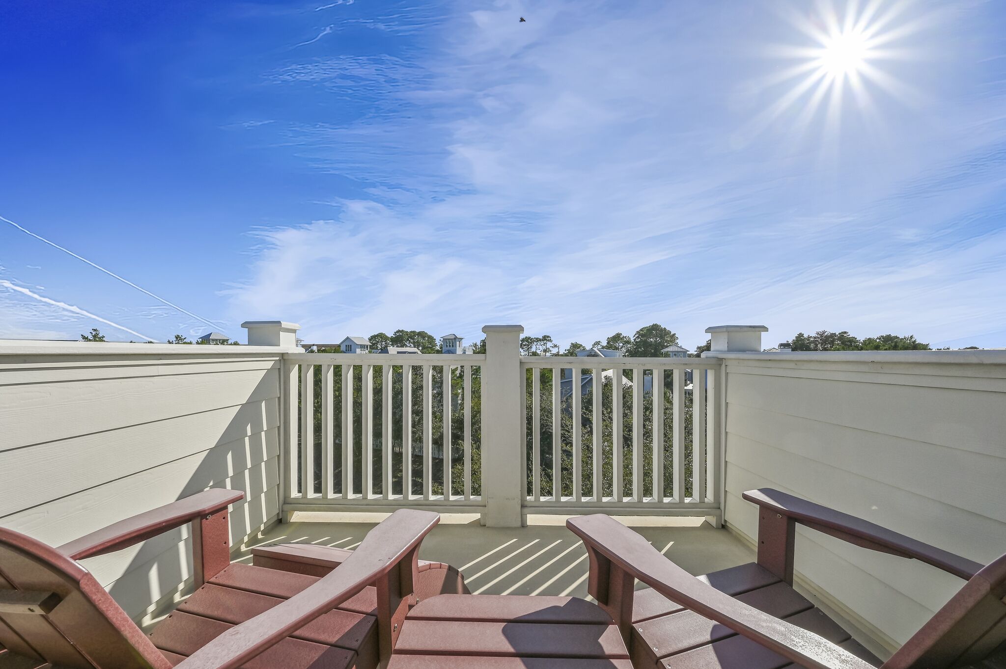 Ein Balkon mit weißen Geländern und roten Stühlen, der auf einen Wohnbereich mit Häusern und Bäumen blickt.
