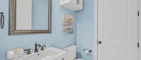 A bathroom with a white sink, a toilet, a mirror, and a cabinet.