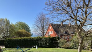 A red house with a sloped roof, surrounded by a well-maintained lawn and a hedge. - New from 2022: beautiful 84 sqm vacation apartment in a top location with partial lake view (Langenargen)
