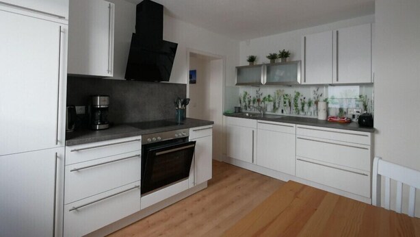 A modern kitchen with white cabinets, a built-in oven, and a countertop with a coffee maker. - New from 2022: beautiful 84 sqm vacation apartment in a top location with partial lake view (Langenargen)