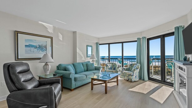 En moderne stue med en læderlænestol, en teal farvet sofa og et sofabord i glas. Store vinduer giver udsigt til havet.