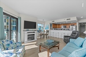 Relax in a spacious living area with a comfortable sofa, flat-screen TV, and fireplace, opening up to a balcony with a view.