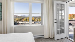 Un dormitorio con un ventanal grande, una puerta que da a un balcón y vistas a un lago y montañas.