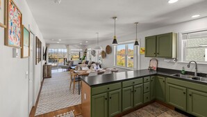 Una cocina moderna con armarios verdes, una encimera negra y un ventanal amplio.