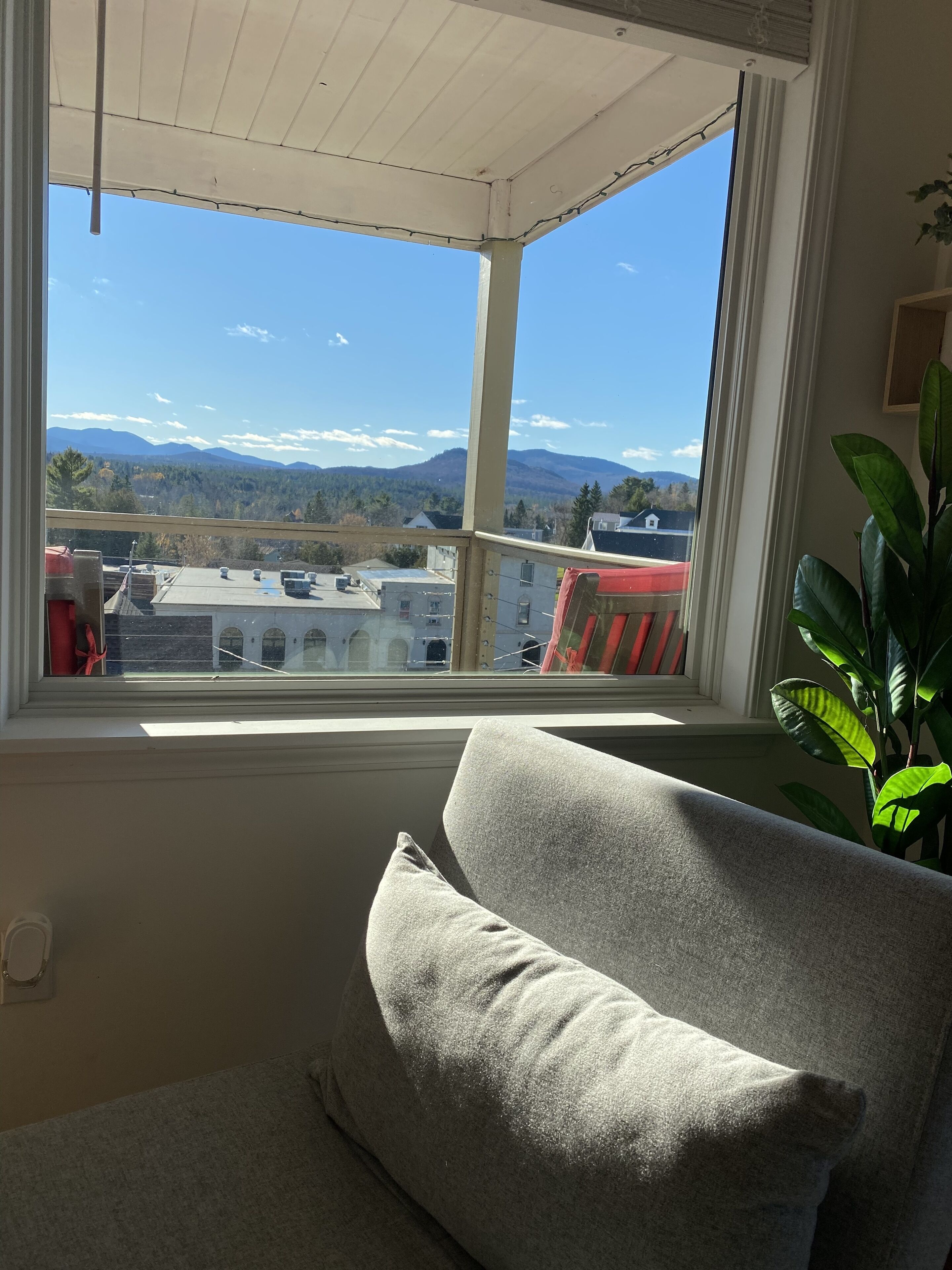 Een kamer met een groot raam, met uitzicht op bergen en een stadsbeeld.