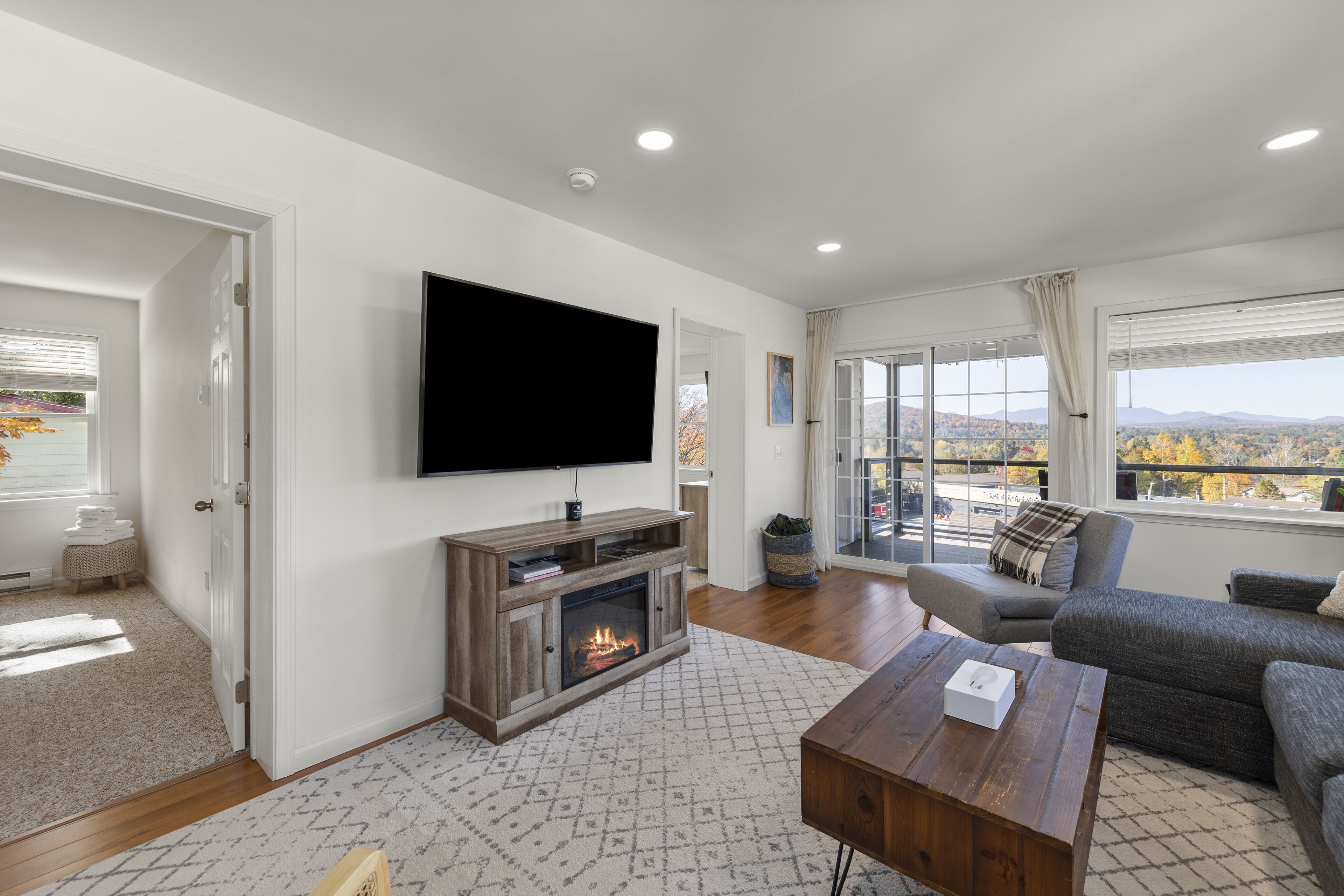 A modern living room with a fireplace, a flat-screen TV, and a large window offering a city view.