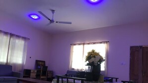 Una sala de estar con un sofá, una mesa de comedor con mantel floreado, un ventilador de techo y una ventana con cortinas.