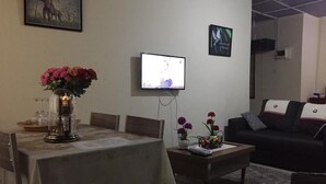 Una sala de estar con una mesa de comedor, un televisor montado en la pared y un sofá.