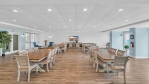 A spacious conference room with a long wooden table and matching chairs, white ceiling with recessed lighting, and light blue walls.