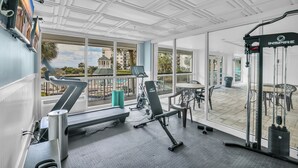 A gym with exercise equipment, large windows, and a view of buildings and trees.