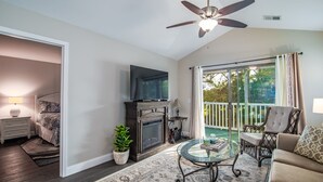 A living room with a fireplace, television, and a balcony with outdoor furniture. - TB 12H  Bedroom/Three Bath unit in True Blue (Pawleys Island)