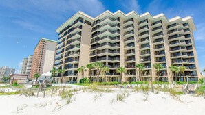 Hotel com vários andares e varandas, próximo a uma praia arenosa.