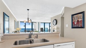 Una cocina con lavavajillas incorporado, un lavaplatos de acero inoxidable y un amplio ventanal con vistas a un balcón.